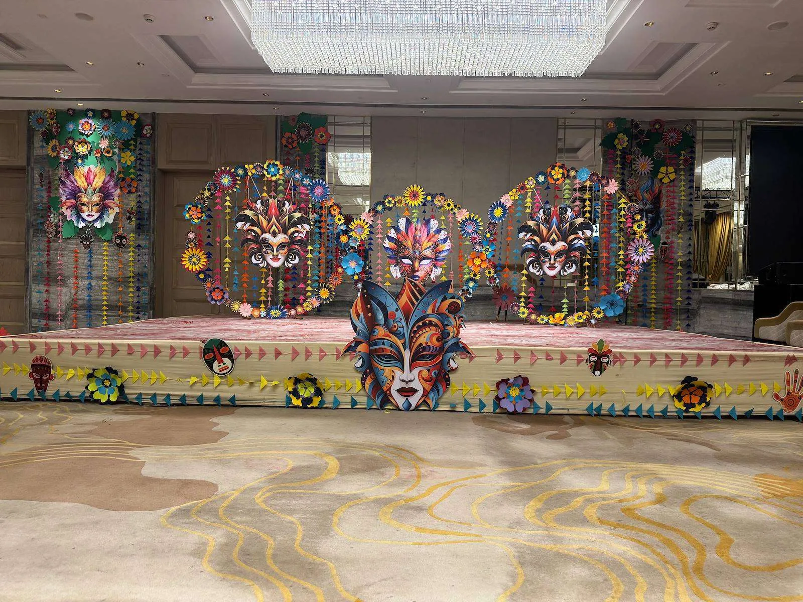 Carnival-themed stage backdrop of paper masks and flowers