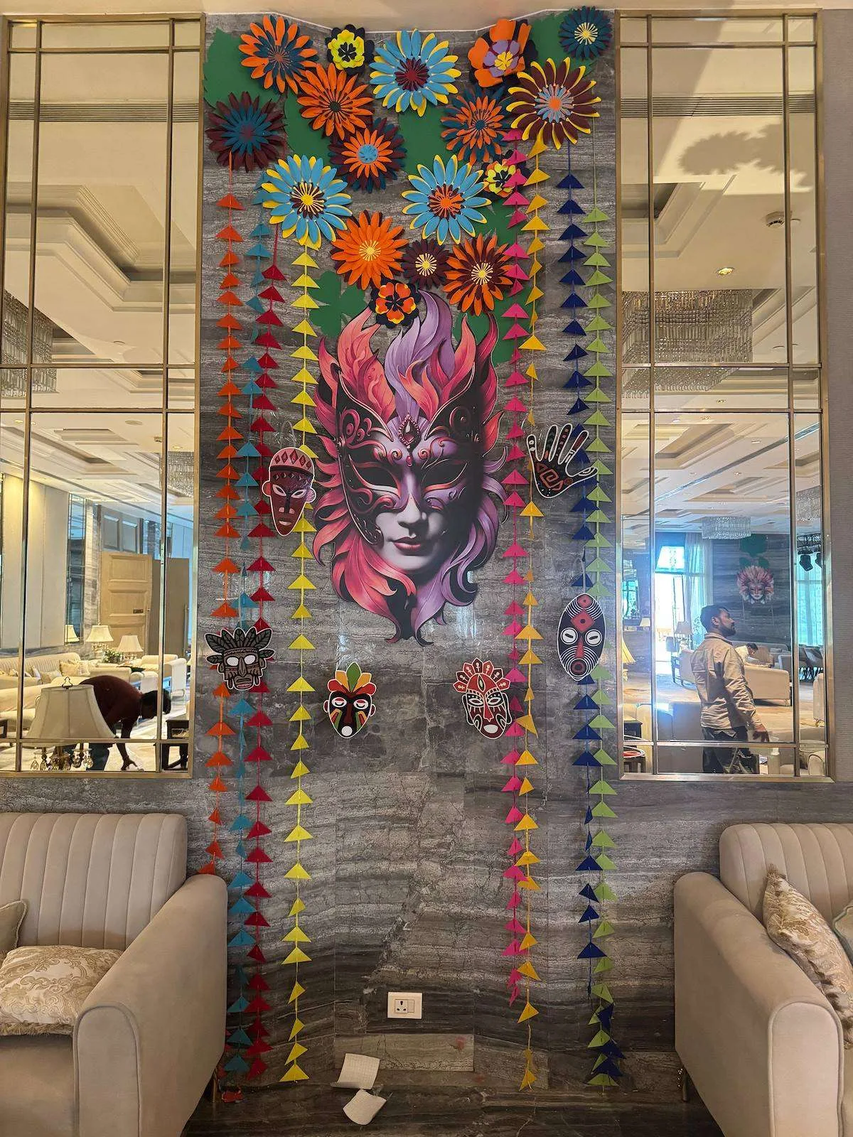 Floor-to-ceiling carnival mask installation with paper garlands in a hotel lobby