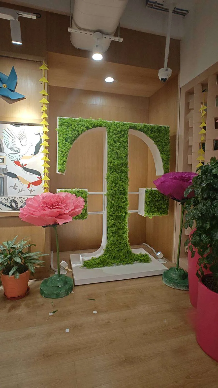 Giant paper rose beside a green moss logo wall